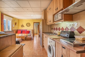 A compact kitchen with wooden cabinets, a built-in microwave, a washing machine, and a toaster. - Apartment 'Picón' with Mountain View, Private Terrace and Wi-Fi (Jérez del Maquesado)