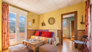 Una habitación con sofá, otomanas, una mesa de centro de madera, un reloj y vistas a través de una ventana.