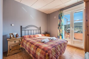A bedroom with a bed, a wooden nightstand, a window with a view, and a balcony door. - Apartment 'Picón' with Mountain View, Private Terrace and Wi-Fi (Jérez del Maquesado)