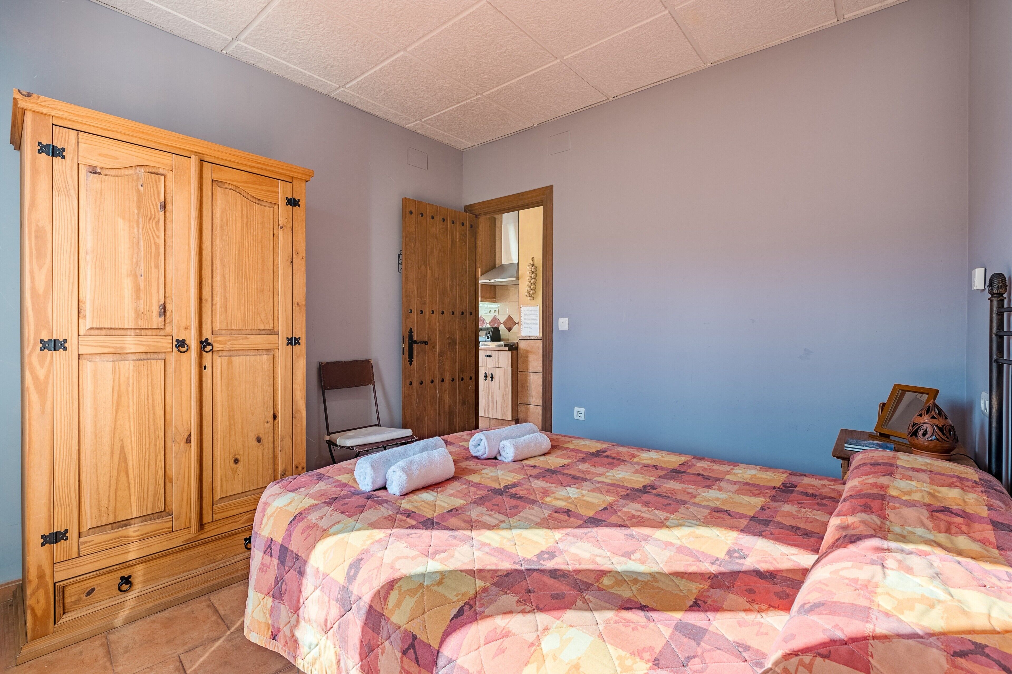 A bedroom with a large wardrobe, a bed with a colorful quilt, and a small table with a mirror and decorative item.