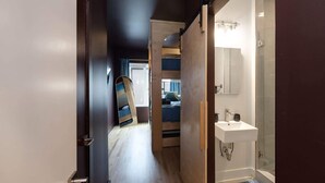 Un pasillo estrecho que conduce a un dormitorio con literas y un baño con lavamanos y ducha.