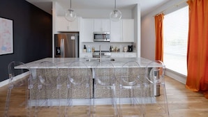A modern kitchen with white cabinets, a stainless steel refrigerator, a microwave, and a large island with a glass top. - 2BR Near DT — Rooftop Deck + Fire Pit + Sleeps 7 (Nashville)