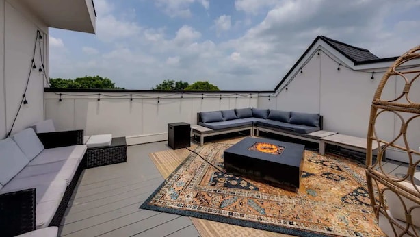 A rooftop terrace with a sectional sofa, a coffee table, a speaker, and a patterned rug. - 2BR Near DT — Rooftop Deck + Fire Pit + Sleeps 7 (Nashville)