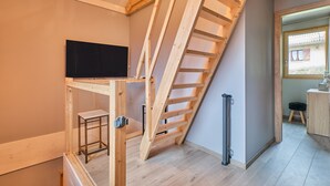 A room with a wooden staircase, a television, and a view of a balcony.