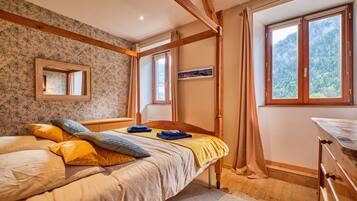 A bedroom with a wooden bed, a mirror, a window with a mountain view, and a dresser.