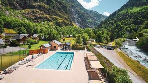 A pool area with lounge chairs, a swimming pool, and a view of a river and mountains.
