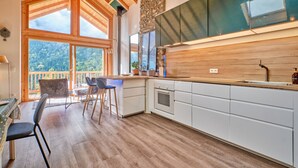 Een moderne keuken met houten balken, grote ramen en uitzicht op het bos.
