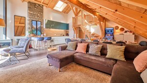 Een ruime loft met hoge plafonds, houten balken, een keukenhoek, een eethoek en een gezellige zithoek met een bank en stoelen.