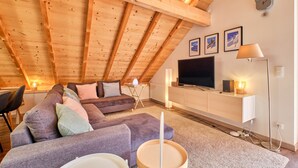 Een gezellig loft slaapkamer met een schuine kap, een groot raam, een flatscreen televisie, een nachtkastje en een lamp.