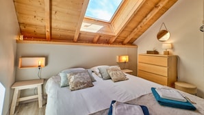 Een slaapkamer met dakraam, een bed met kussens, nachtkastjes, een kaptafel en een spiegel.