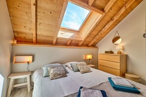 Ein Schlafzimmer mit Dachfenster, einem Bett mit Kissen, Nachttischen, einer Kommode und einem Spiegel.