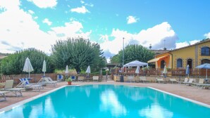 A swimming pool with lounge chairs and umbrellas, surrounded by a wooden fence and trees. - Stunning home in Sassoferrato (Sassoferrato)