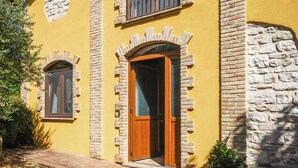 A yellow building with two wooden doors and windows, surrounded by stone walls and greenery. - Stunning home in Sassoferrato (Sassoferrato)