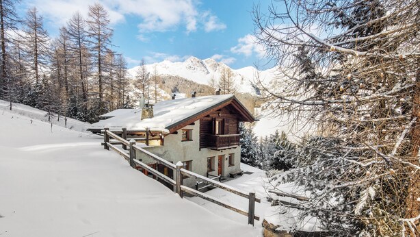 Une cabane en bois dotée d’un balcon, entourée d’arbres et de montagnes couverts de neige.