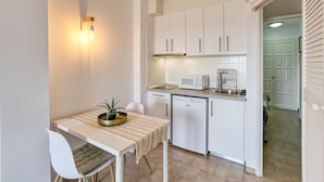 Une cuisine compacte avec des meubles blancs, un four à micro-ondes, un lave-vaisselle et un petit coin repas comprenant une table et une chaise.