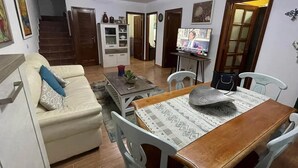 A living room with a sofa, dining table, chairs, a TV, and a staircase leading to another room. - Abades Beach Houses by EstrellaDelNorte (Arico)