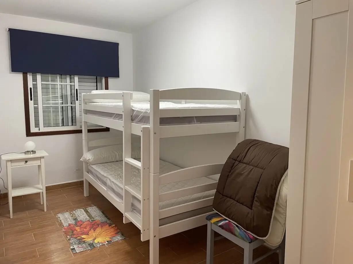 Dormitorio con literas, una ventana, una mesita y una silla.