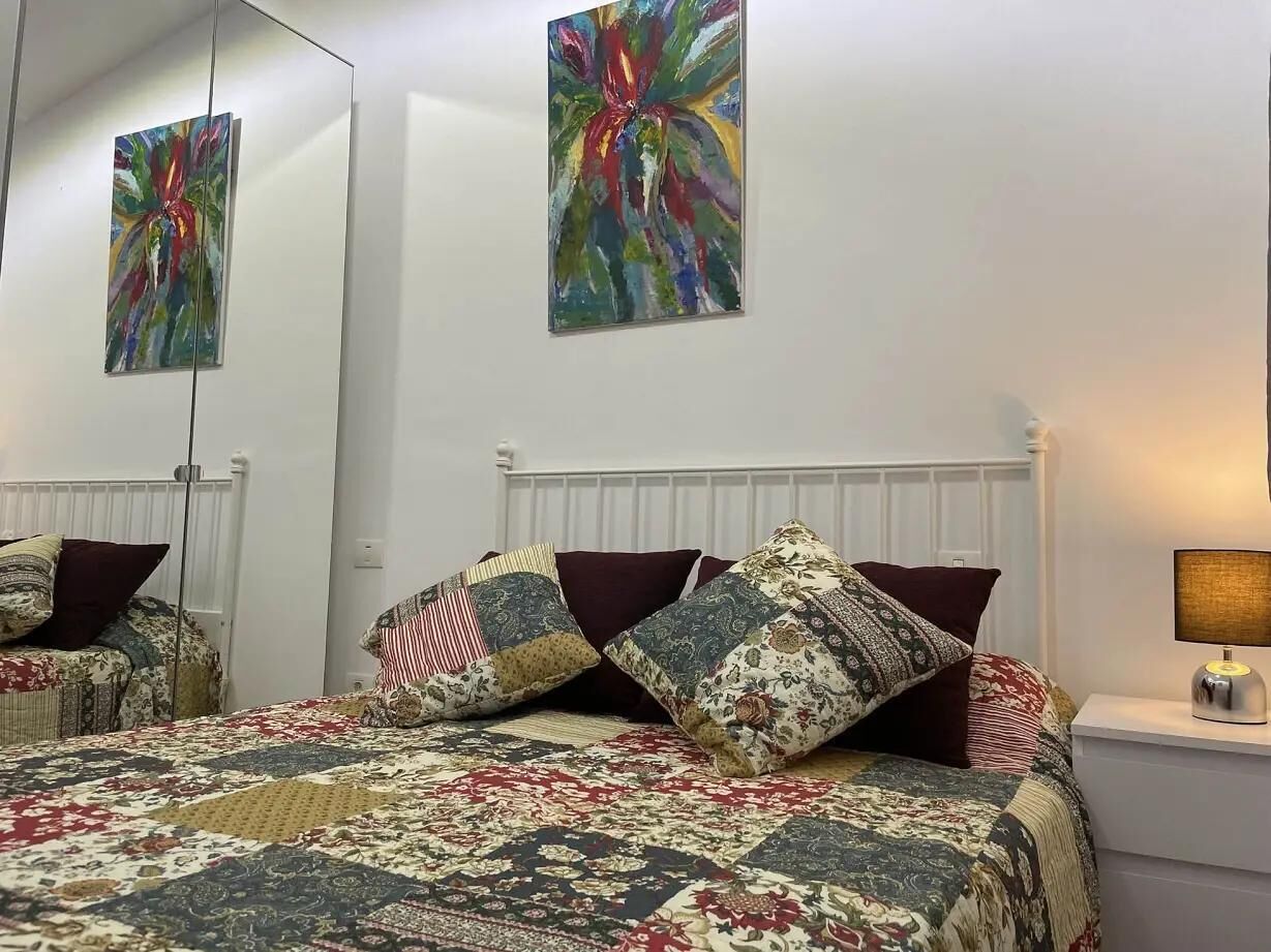 Een slaapkamer met een bed, gestreepte kussens, een bedlampje en twee abstracte schilderijen aan de muur.