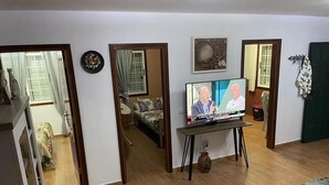 A living room with a television displaying a news program, a sofa, a coffee table, and a patterned rug. - Abades Beach Houses by EstrellaDelNorte (Arico)