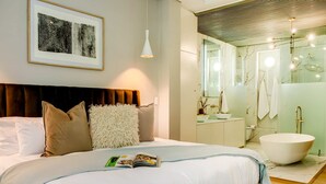 Une chambre d’hôtel moderne avec un grand lit, une baignoire blanche et une salle de bain dotée d’une douche en verre.