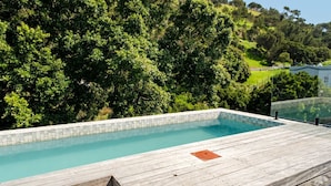 Une terrasse en bois avec une piscine, entourée d’une végétation luxuriante et de collines.