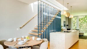 Une cuisine moderne dotée d’un îlot central, d’un coin repas avec une table ronde et d’un escalier au design original.