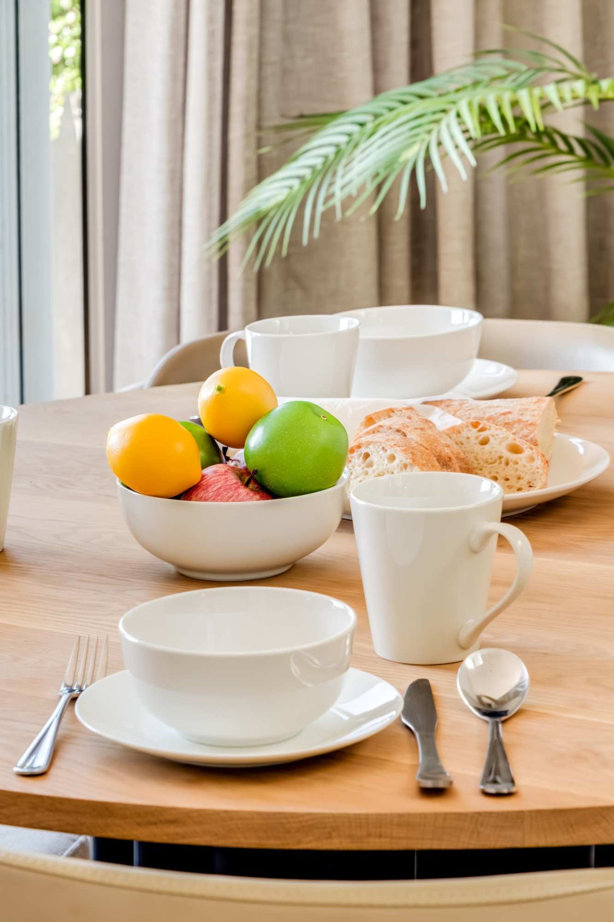 Mesa de madeira com uma tigela de fruta, uma xícara de café e um prato de pão.