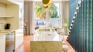 Une cuisine moderne dotée d’un îlot en marbre, d’un coin repas avec une longue table et d’une vue sur un balcon agrémenté de plantes.