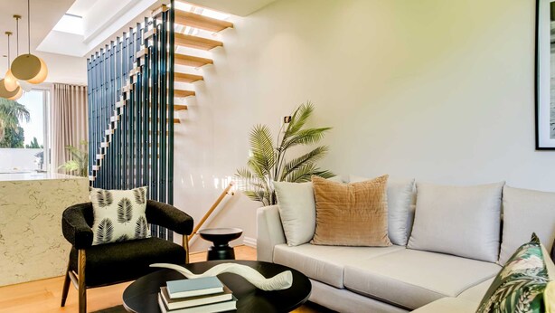 A modern living room with a sofa, a black coffee table with books, a patterned armchair, and a tall plant. - Ultimate Escape in Vibrant De Waterkant at Ishani (Cape Town)