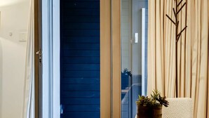 Ein modernes Zimmer mit einer Schiebeglastür, die auf einen Balkon führt, einem runden Tisch mit Topfpflanze und einem strukturierten beigen Sessel.