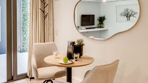 Ein Zimmer mit einem runden Tisch, zwei Stühlen, einem Spiegel, einem Fernseher und einer Pflanze.