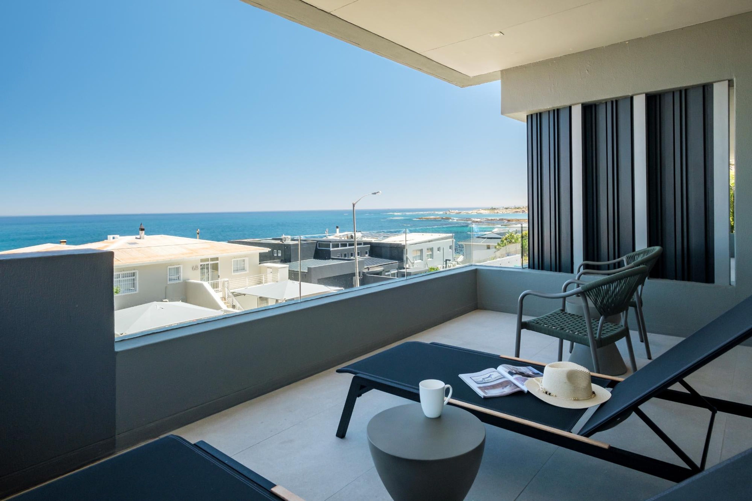 Un balcon avec vue sur la mer, un fauteuil de relaxation, une petite table et un chapeau.