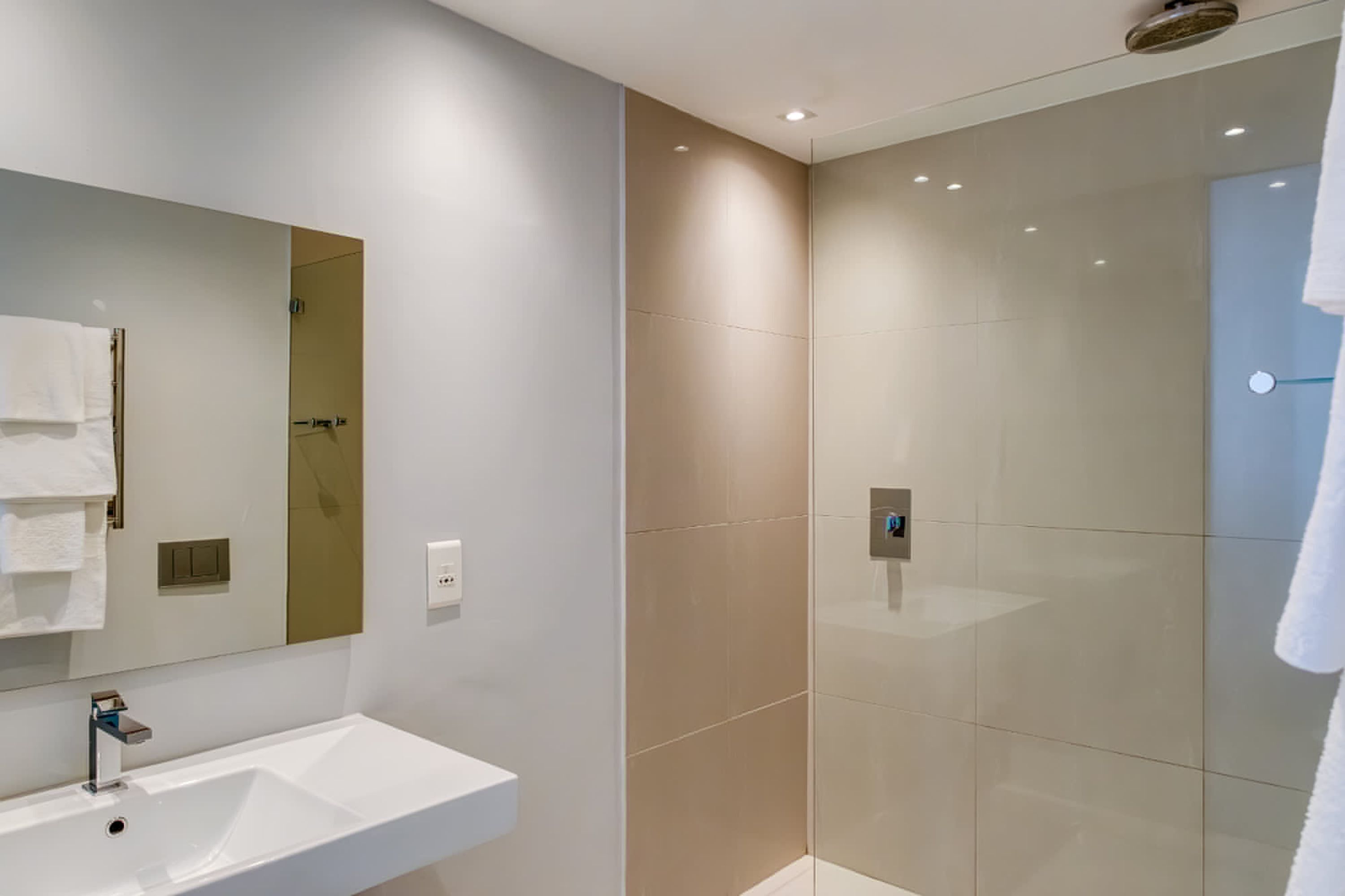 A modern bathroom with a white sink, a mirror, and a glass-enclosed shower.