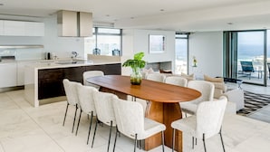 Una cocina moderna con armarios blancos, una mesa de comedor de madera y vistas al océano.
