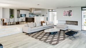 Una sala de estar moderna con un sofá, una mesa de centro y un otoman, un comedor con sillas, y una cocina equipada.