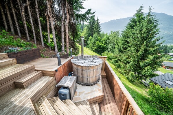 A wooden deck with a hot tub and a sauna, surrounded by trees and a mountain view.