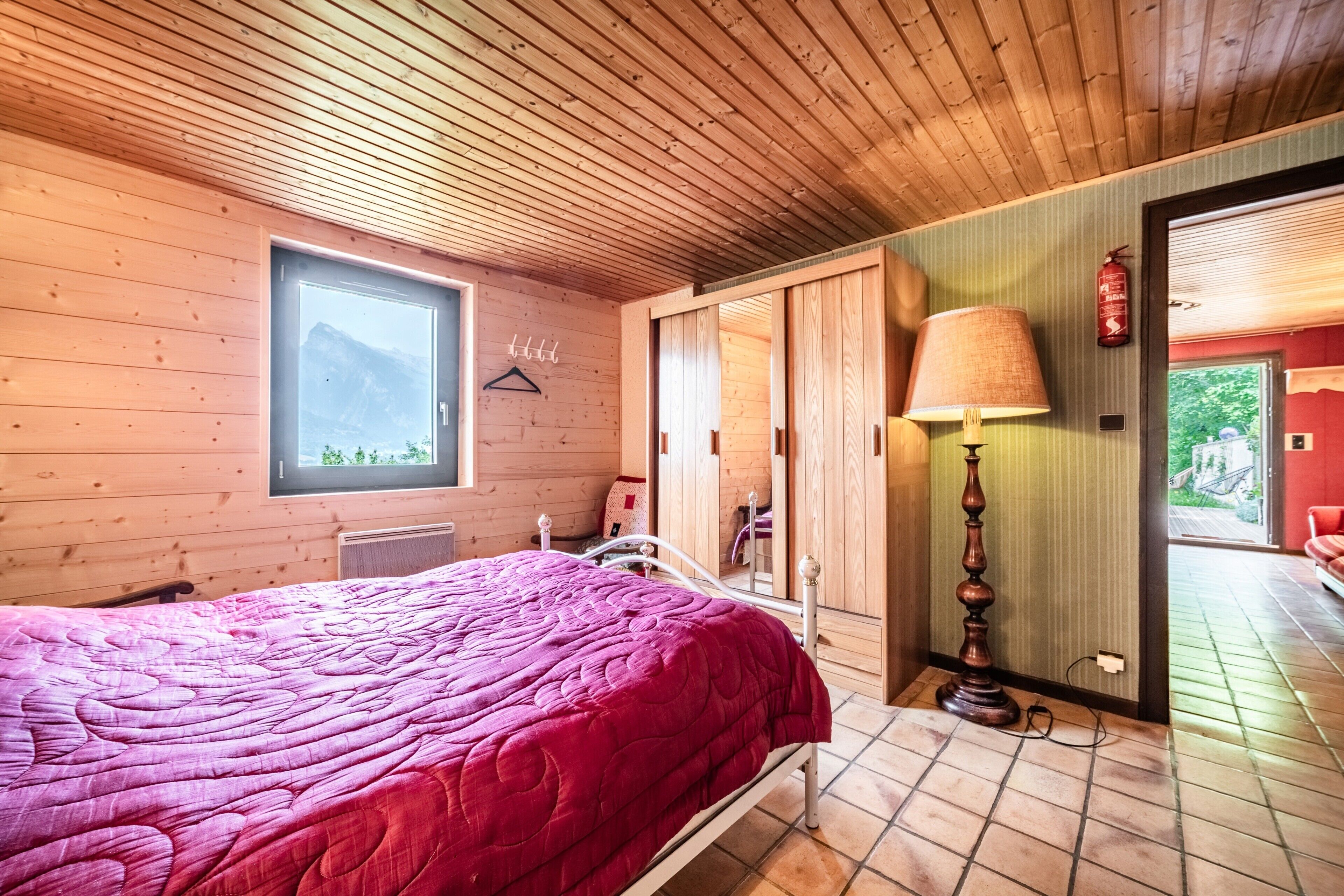 Dormitorio con paneles de madera, una cama, una ventana, una lámpara y vistas al exterior.