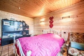 A wooden-paneled room with a bed, a bookshelf, and a wall-mounted light fixture.