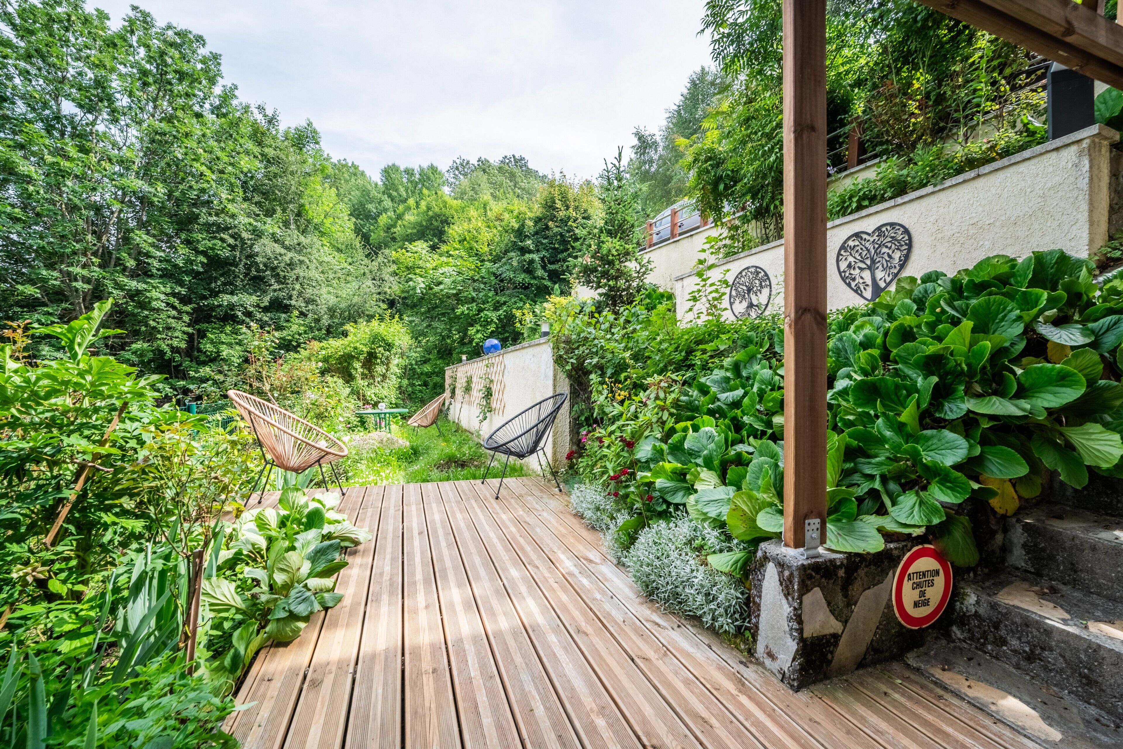 A wooden deck with a hammock, surrounded by lush greenery and a heart-shaped wall mural.
