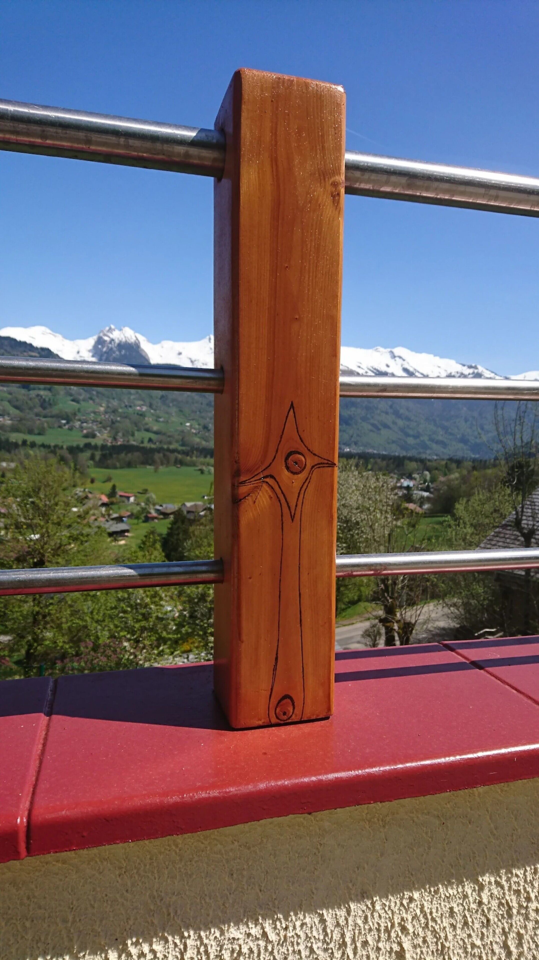 Ein Holzboden mit einem geometrischen Muster, einem Metallgeländer und einer roten Plattform mit einer Berglandschaft im Hintergrund.