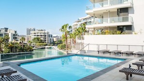Un hotel moderno con piscina en la azotea, palmeras y vistas a otros edificios.