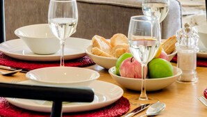 Una mesa de comedor dispuesta con platos, vasos, pan y un bol de fruta.