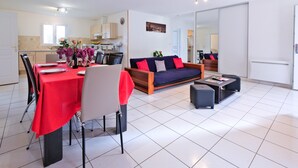 Una sala moderna con un sofá, una mesa de comedor con sillas y una cocina al fondo.