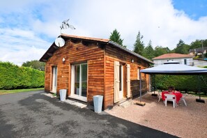 A wooden cabin with a covered patio, a satellite dish, and a gravel driveway.