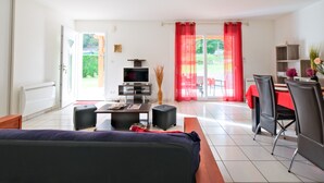 Een moderne woonkamer met een bank, een televisie, een eettafel met stoelen en een rood gordijn.