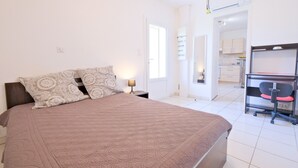 Een slaapkamer met een bed, twee kussens met een patroon, een bedlamp en uitzicht op een keuken.
