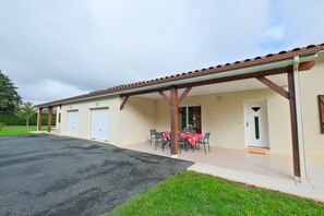 Un bâtiment doté d’un patio couvert, d’une table avec des chaises et d’une porte.
