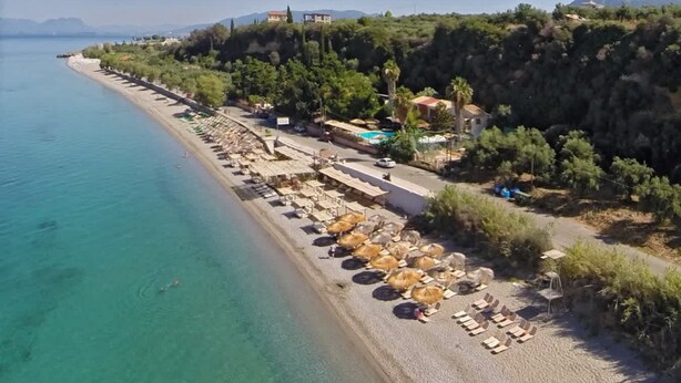 Una playa con tumbonas y sombrillas, una piscina y edificios en una colina.