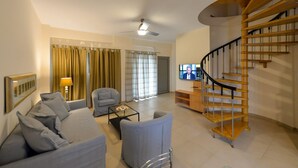 Una sala de estar moderna con un sofá gris, una mesa de centro, un televisor y una escalera espiral de madera.