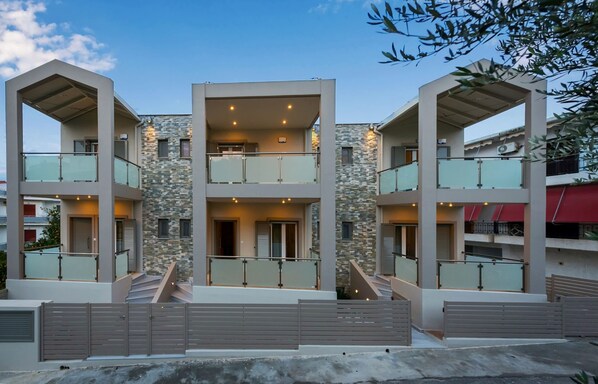 A modern multi-story residential building with balconies, a stone facade, and a gated entrance.